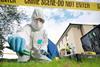 A crime scene technician wearing white overalls and latex gloves collects evidence from a lawn with some tweezers