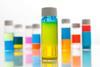 A glass vial with a white lid containing a green liquid that is separating between blue at the top and yellow at the bottom. Other vials of different two-colour liquids are behind.