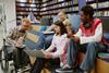 A diverse group of sixth form students in casual clothes gather around a laptop