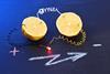 Two halves of a lemon wired together and to a red bulb that is glowing. On the table written in chalk is a plus and minus sign and a lightning bolt