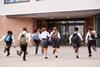 Young high school students in school uniform carrying backpacks run towards the school entrance.