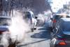 A photograph of queuing urban traffic, showing steam rising from car exhaust pipes