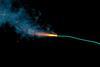 A long green-blue fuse burns against a black background, giving off orange sparks and grey smoke
