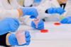A photograph of students sitting around a table and wearing protective gloves while making slime in plastic pots