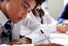 A photograph of a male student in school uniform working individually at a desk
