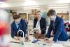 A photograph of two secondary school students and their teacher smiling while discussing an experiment in a chemistry lesson