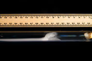 A ruler against a glass tube with smoke forming inside