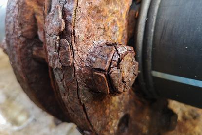 A close-up photograph of a corroded carbon steel structure on a pier, with visible rust
