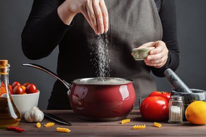 chef adding salt to a saucepan of pasta
