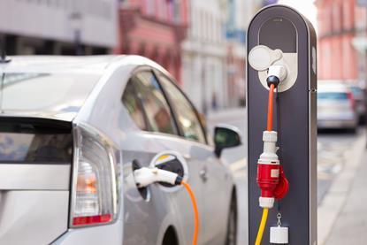 A photograph of an electric car connecting to a charging station at the side of a street