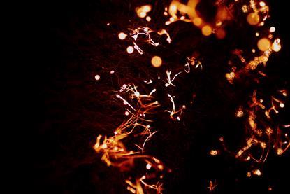 A close-up photograph of strands of iron wool burning white, orange and red against a dark background