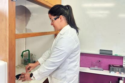Orla Casby working as a science teacher wearing a lab coat and safety glasses working at a fume hood