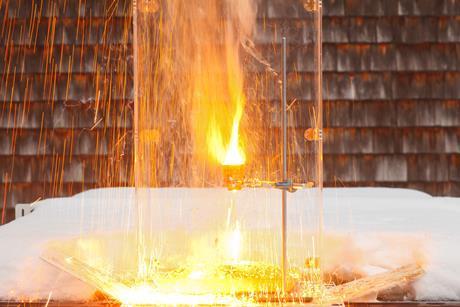 A sparks and bright flash of hot material in a terracotta flowerpot held in a laboratory clamp and stand. The set up is outside with some snow behind a protective clear screen