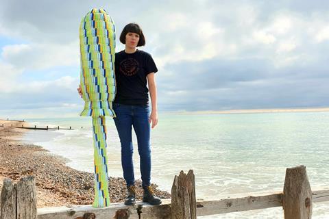 A photo of a woman on a beach with a giant tampon applicator made of giant tampon applicators