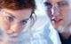 Two students wearing safety glasses and lab coats closely observe a reaction