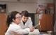 An image showing a female student burning magnesium on a Bunsen burner using tongs while a male classmate is watching the flame created. Both are wearing safety goggles