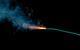 A long green-blue fuse burns against a black background, giving off orange sparks and grey smoke