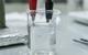Electrode set-up to anodise titanium in a beaker with red crocodile clip holding titanium and black crocodile clip holding wire in an electrolyte solution