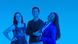 Three DW employees smile into the camera against a blue background