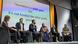 Six panelists on a stage, the slide in the background reads "Journalism is a public good but it's not funded like other public goods"