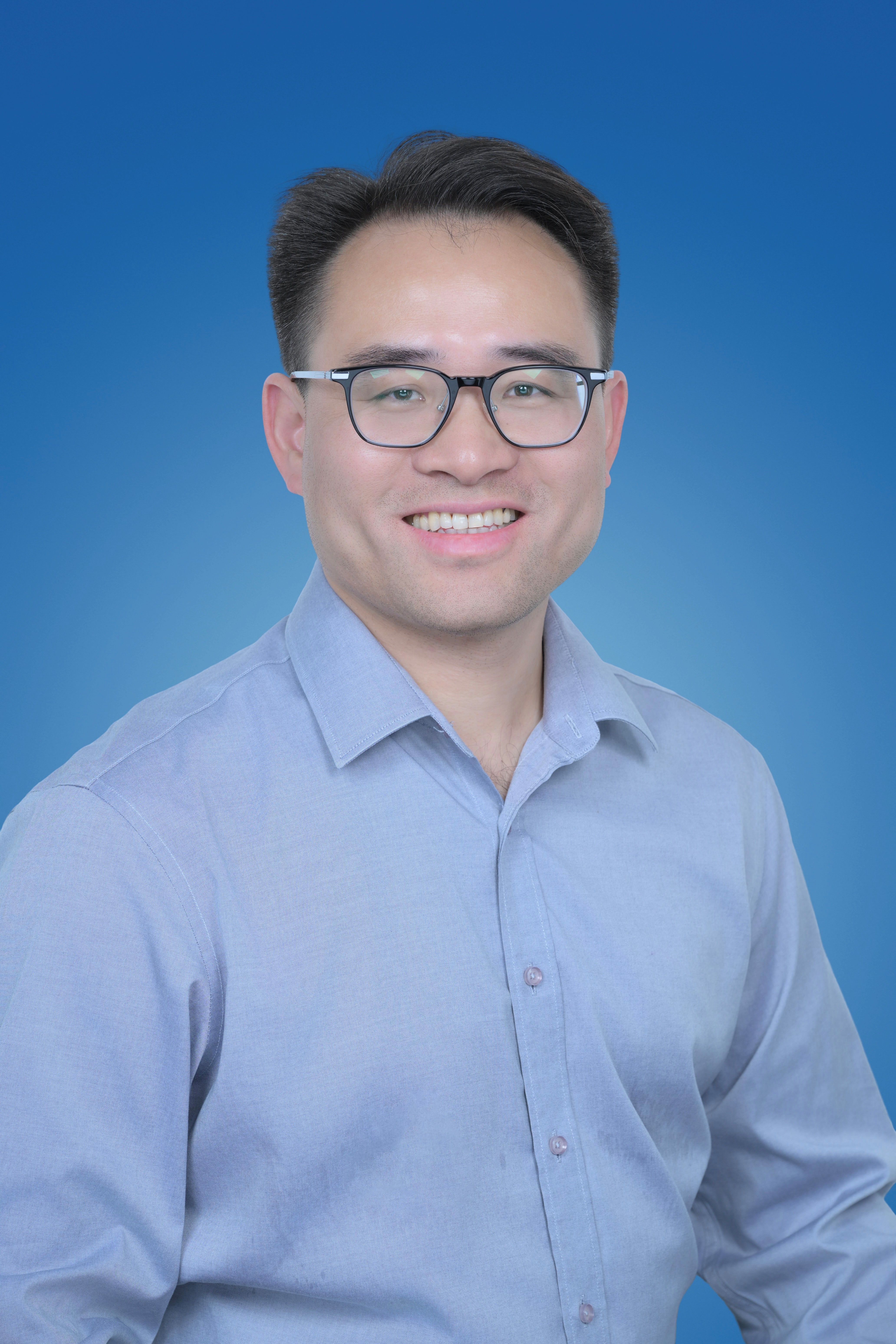 Jun Cheng smiling at camera wearing a blue shirt and glasses
