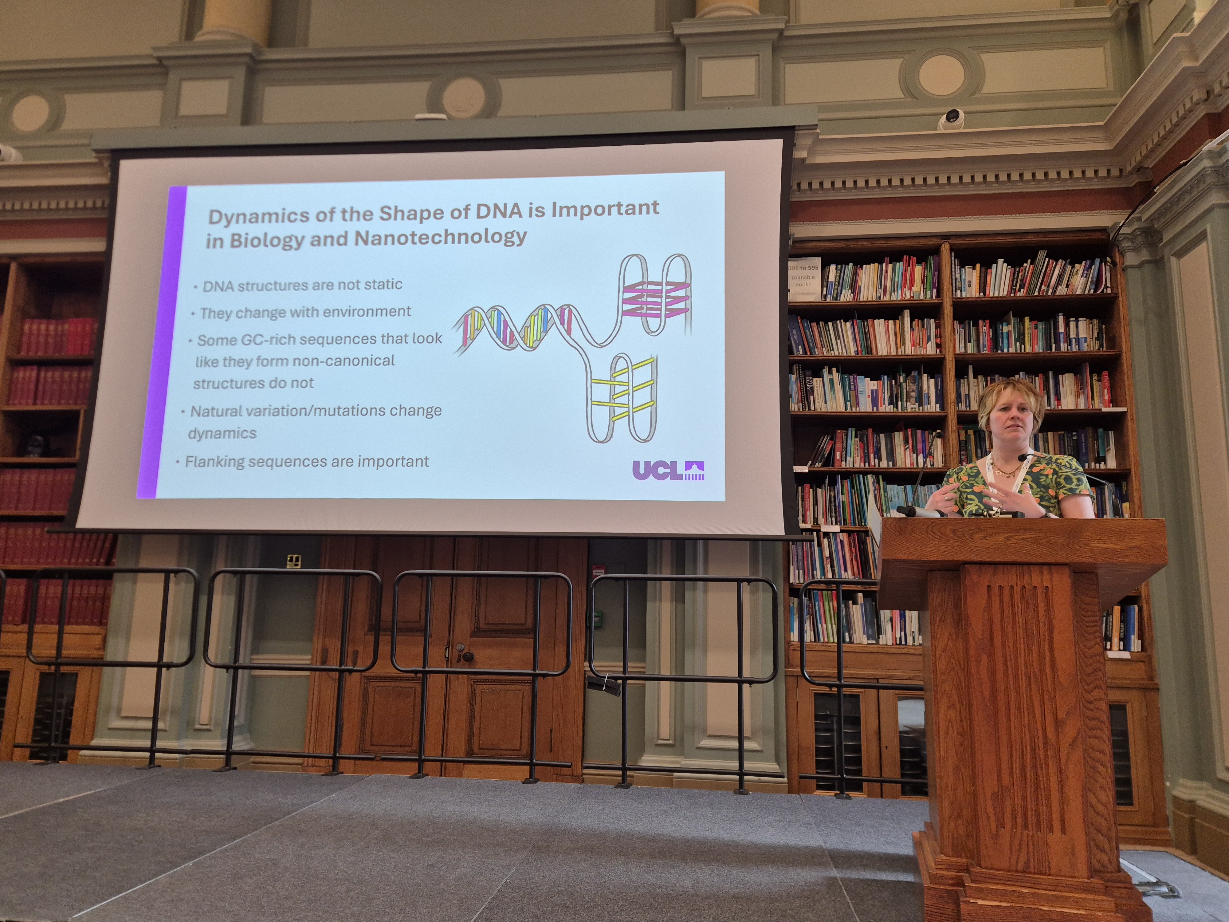 Professor Zoe Waller stands at a podium in front of a large screen