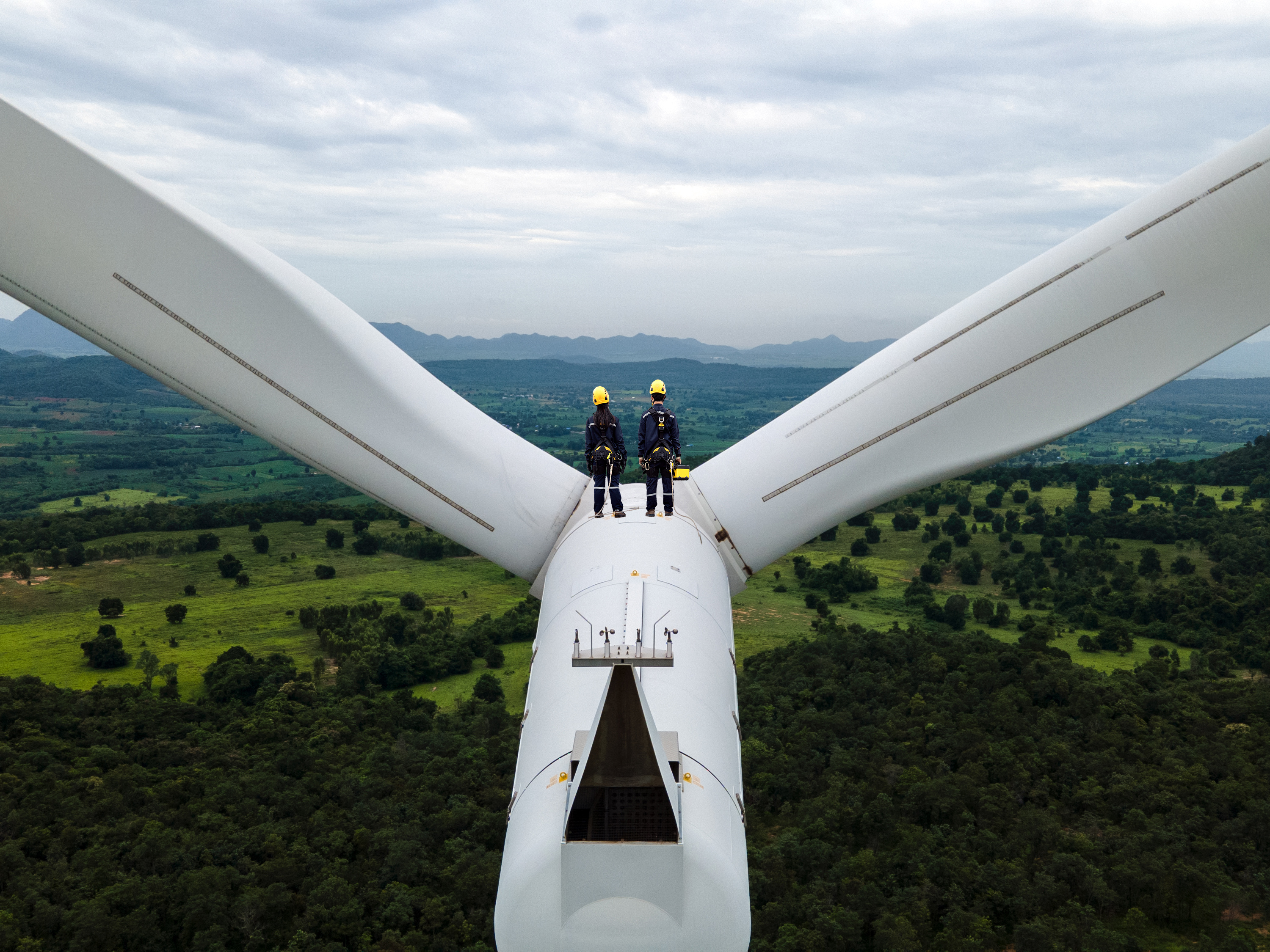 two people standing on top of a wind turbine looking out to the horizon