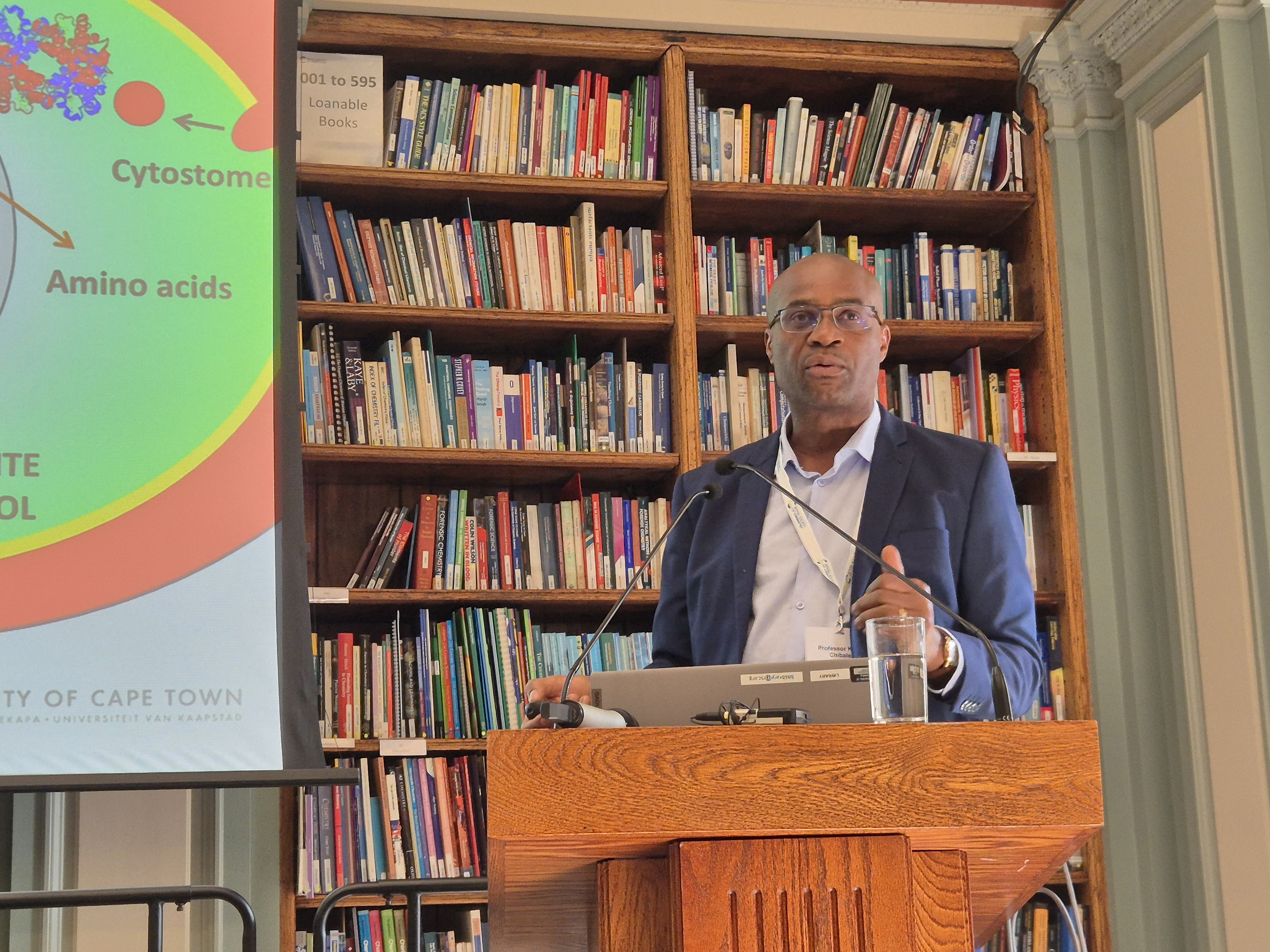 Professor Kelly Chibale stands at a lectern and faces a crowd (out of shot)