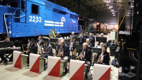 A big band performs swing-era music beside a bright blue Conrail locomotive inside the Railroad Museum of Pennsylvania, surrounded by vintage trains during the Trains & Troops weekend celebration.