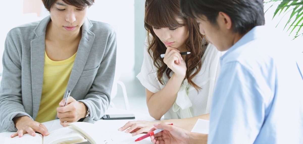 男女3人がノートを開き、ペンを手に課題を検討している。