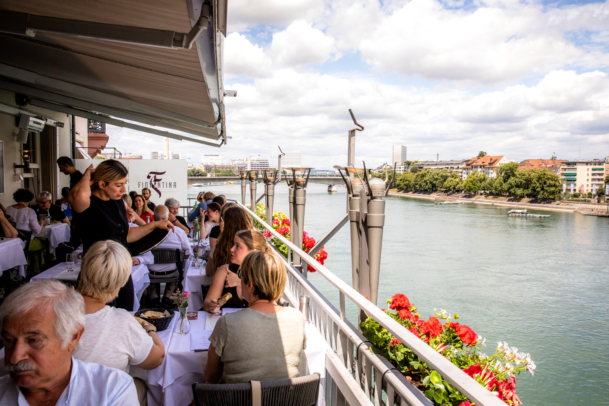 Gäste essen auf der Terrasse des Restaurants Fiorentina am Blumenrain in Basel bei schönem Wetter mit Blick auf den Rhein.