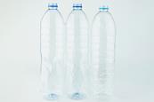 Three clear empty plastic drink bottles, against a plain white-grey background