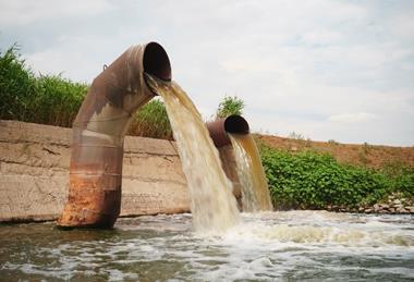 Wastewater from two large rusty pipes merge into the river in clouds of steam
