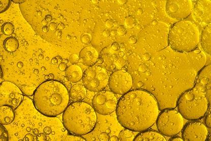 A close-up photograph showing circles of yellow-gold cooking oil floating on water