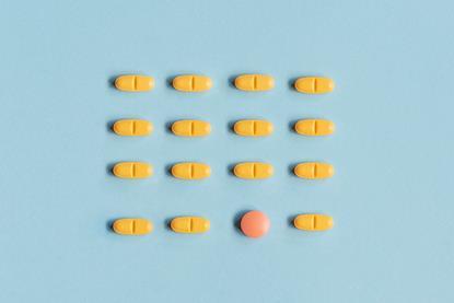 A photograph of yellow-orange pills arranged in rows on a blue background; in the bottom row, a different, red pill stands out