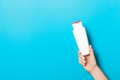A photograph showing a woman's hand holding a white plastic cosmetics bottle against a blue background.