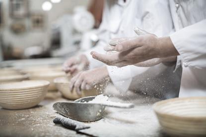 A photograph of a baker's hands covered in flour, as the baker prepares ceramic bowls for baking bread
