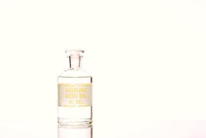 A photograph of a labelled glass bottle containing dilute sulfuric acid against a plain background
