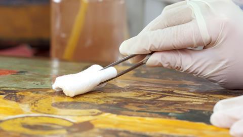 Close of gloved hands cleaning an old painting