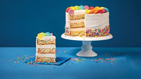 A colourful cake on a cake stand with a piece taken out to show the colourful candy inside
