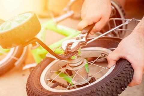 An adult using a spanner to remove training wheels from a child's bike