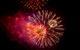 A photograph of red, orange and gold fireworks exploding against the night sky, giving off smoke that appears to have a red colour