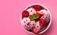 Three pink ice cream scoops covered in raspberries and strawberries