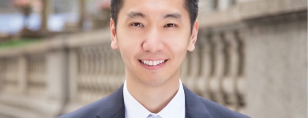 Headshot of Robert Chen, WG’19, outdoors smiling in a blue suit, with a stone building in the background.