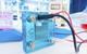 A photograph of a transparent blue hydrogen fuel cell in a laboratory, connected to a power source