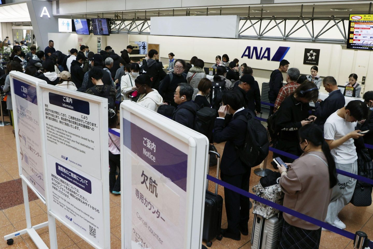 Passengers wait in line at All Nippon Airways' counter at Haneda airport in Tokyo on Saturday. A sign, right, reads "Flight cancellation counter."