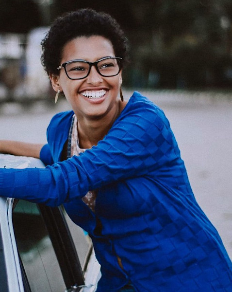 Une femme aux côtés de sa voiture est heureuse.