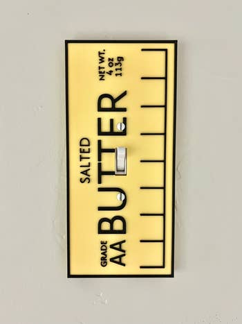 Light switch cover resembling a stick of salted butter, displays text