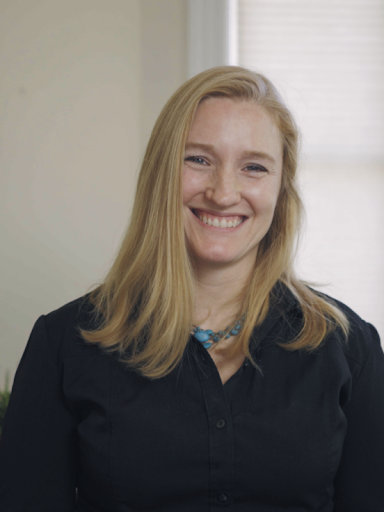Woman with long blond hair, wearing a black shirt and turquoise necklace is posed smiling