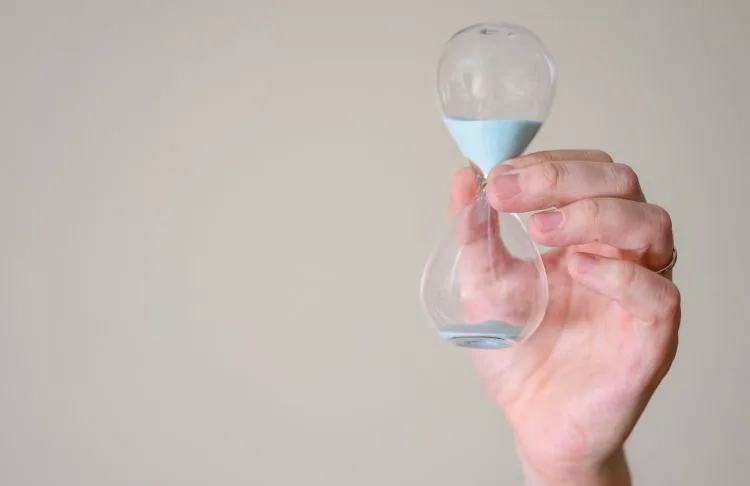 person holding hour glass with blue sand falling through it